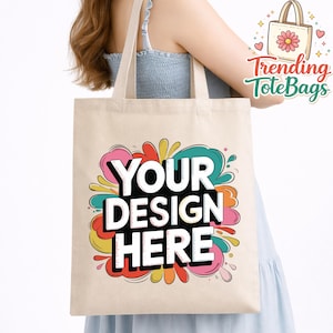 May include: Beige tote bag with the text "YOUR DESIGN HERE" in white letters on a black background, surrounded by colorful splashes. The bag has long, beige handles and the words "Trending ToteBags" in red and green.