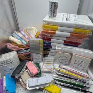 May include: A collection of stationery supplies including a stack of colored notebooks, various sticky notes in heart and square shapes, thin index tabs, several plastic-cased reading lights in assorted colors, and a set of multi-colored ballpoint pens.