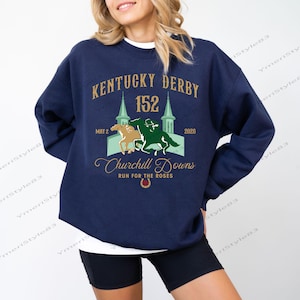 May include: Navy blue sweatshirt featuring the text "Kentucky Derby 152" with a graphic of two horses racing. The design includes the words "Churchill Downs" and "Run for the Roses". The sweatshirt is a casual style.