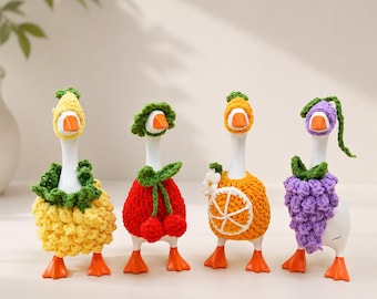 Könnte beinhalten: Vier weiße Gänsefiguren aus Keramik, die gehäkelte Outfits im Fruchtdesign tragen. Die erste trägt ein gelbes Ananaskostüm, die zweite ein rotes Kirschenoutfit, die dritte ein Orangenscheiben-Design und die vierte ein violettes Traubenensemble.