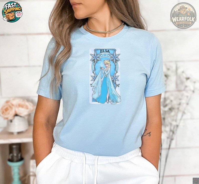 A woman wearing a light blue tee with an Elsa graphic featuring the Disney character in an ice-blue gown surrounded by ornate snowflake designs.