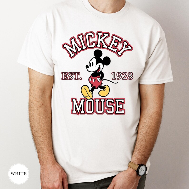 K&ouml;nnte beinhalten: Wei&szlig;es T-Shirt mit einer Mickey Mouse-Grafik und dem Text "MICKEY MOUSE EST. 1928" in Rot und Wei&szlig;. Die Zeichentrickfigur ist in ihrem klassischen Outfit mit roten Shorts und gelben Schuhen dargestellt.