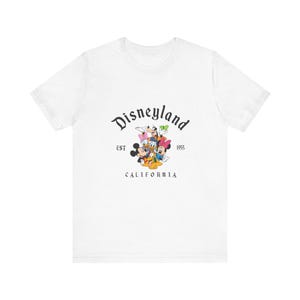 White unisex tee featuring classic Disney characters with "Disneyland EST 1955 California" text graphic centered on chest.