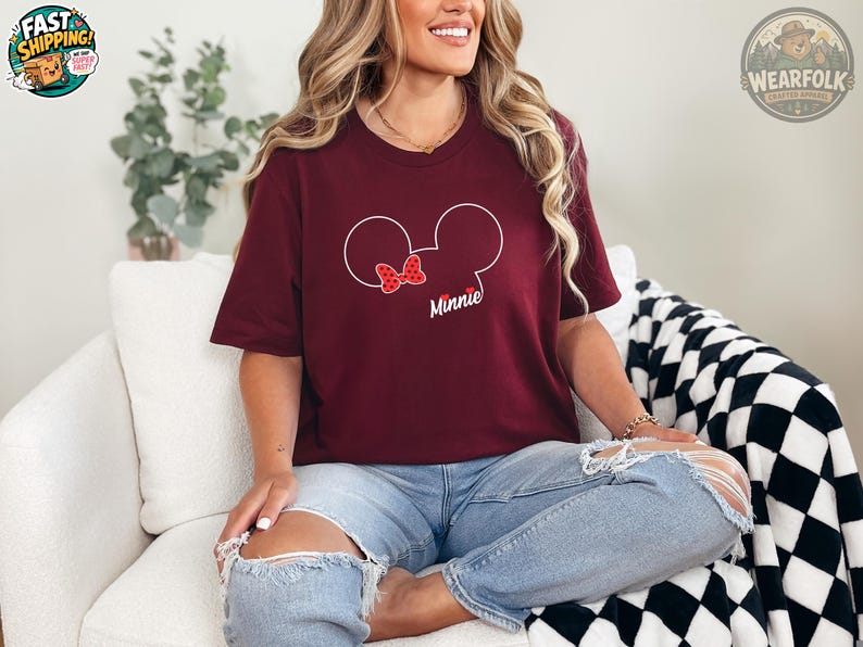 A woman wearing a burgundy tee with a Minnie Mouse head graphic featuring a red polka-dot bow and the word "Minnie" in white text.