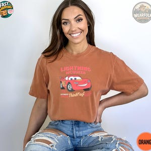 A woman wearing a rust-colored tee with a red Lightning McQueen car graphic and pink text reading "Lightning McQueen Ultimate Speed Think Fast.