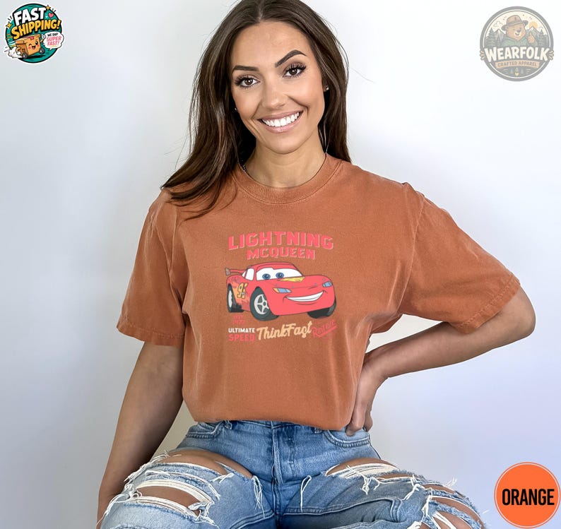 A woman wearing a rust-colored tee with a red Lightning McQueen car graphic and pink text reading "Lightning McQueen Ultimate Speed Think Fast.