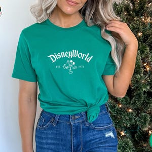 Woman wearing a kelly green Bella Canvas tee with white "DisneyWorld EST 1971" text and Mickey graphic on the front.