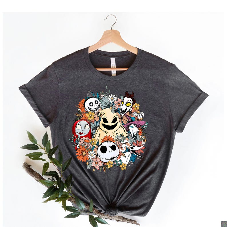 Woman wearing a dark gray tee with a colorful graphic of skeleton characters surrounded by orange and pink flowers and autumn leaves.