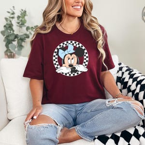 Woman wearing a maroon tee with a Minnie Mouse graphic inside a black and white checkered circle on the front.