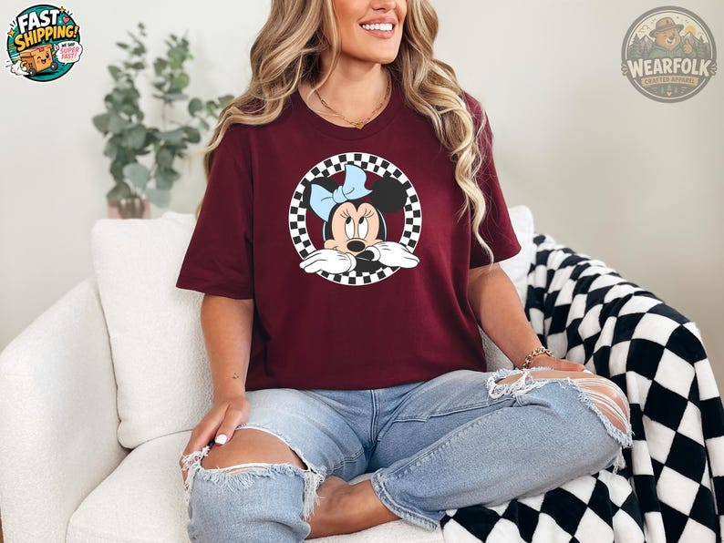 Woman wearing a maroon tee with a Minnie Mouse graphic inside a black and white checkered circle on the front.