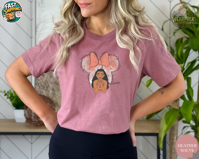 A woman wearing a heather mauve tee with an illustration of Moana's face wearing a polka dot bow and the text "Moana" below.