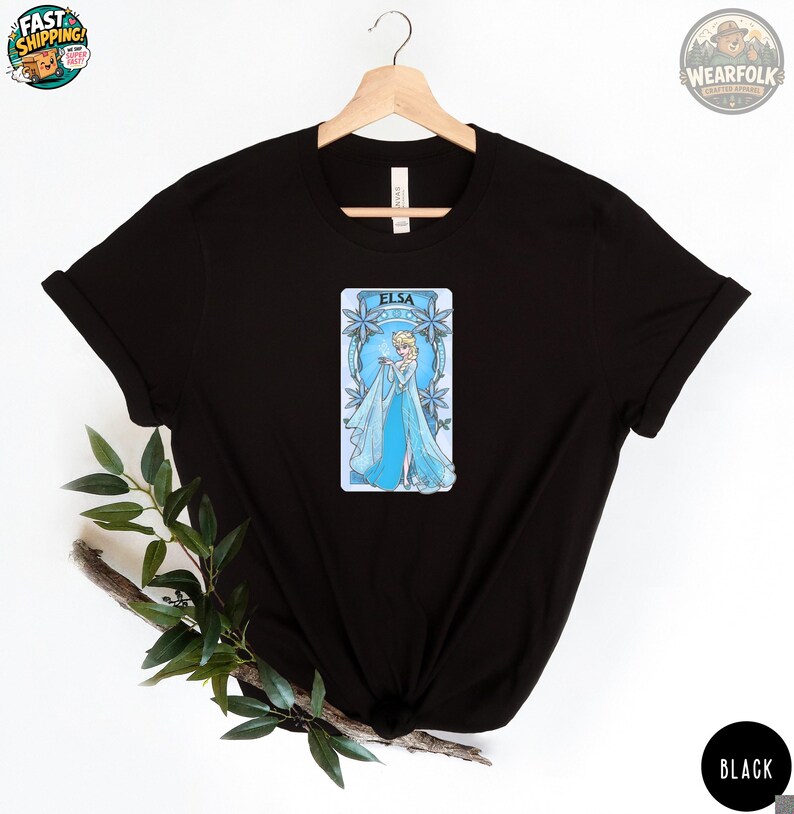 A woman wearing a black Bella Canvas tee with a centered blue and white graphic of Elsa in an ornate ice-themed frame with snowflake details.