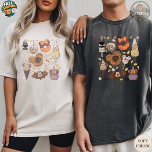 A woman and man wearing matching Bella Canvas tees with Halloween candy and treats graphic including skull donuts, ice cream cones, and candy corn illustrations.