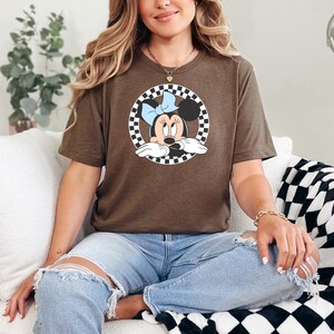 Woman wearing a brown Bella Canvas tee with Minnie Mouse graphic inside a black and white checkered circle design on the front.