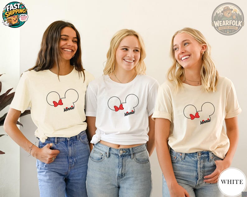 Three women wearing cream and white tees with Minnie Mouse head graphic featuring a red polka dot bow and "Minnie" text.