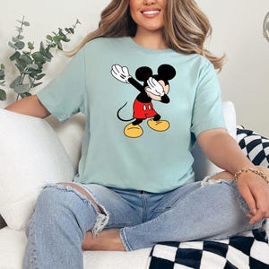 A woman wearing a light blue tee with a classic Mickey Mouse graphic featuring the character in his red shorts and yellow shoes with white gloves.