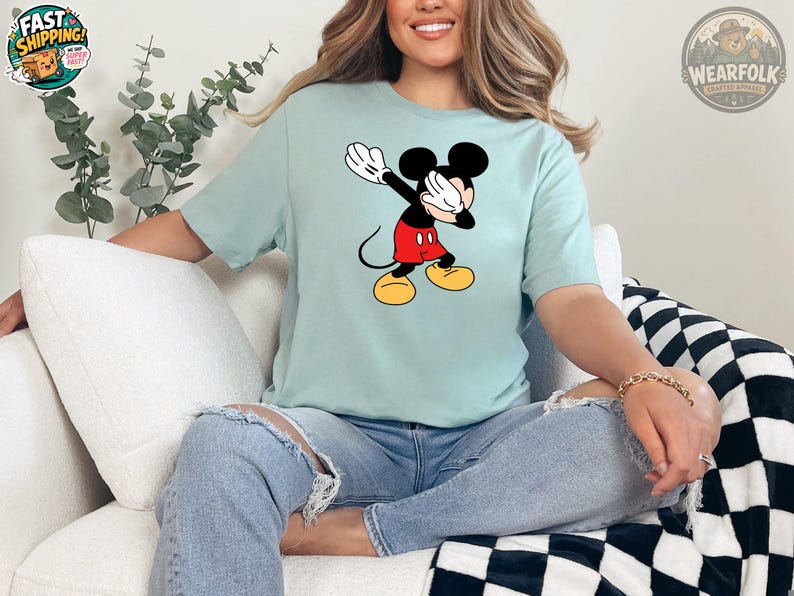 A woman wearing a light blue tee with a classic Mickey Mouse graphic featuring the character in his red shorts and yellow shoes with white gloves.