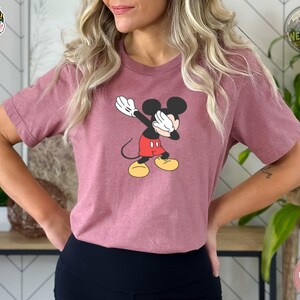 A woman wearing a heather mauve tee with a classic Mickey Mouse graphic showing the character in his iconic red shorts and yellow shoes with white gloves.