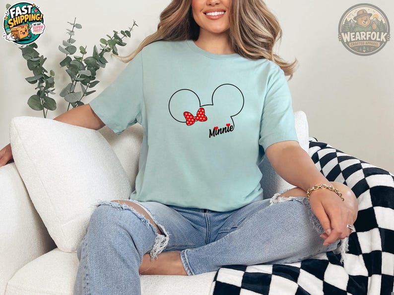 Woman wearing a light blue tee with a Mickey Mouse head graphic featuring a red polka dot bow and the word "Minnie" in black script text.