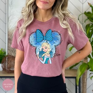 Woman wearing a heather mauve tee with Elsa from Frozen inside a blue polka-dot Mickey Mouse ears graphic that says 'Elsa'.