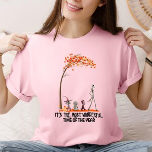 A woman wearing a pink tee with an autumn tree graphic and characters below text reading "It's the Most Wonderful Time of the Year".