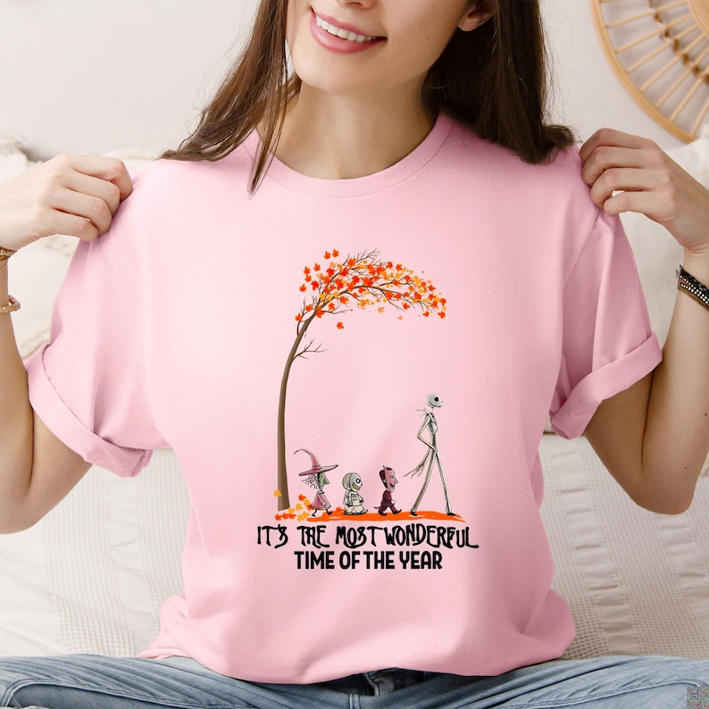A woman wearing a pink tee with an autumn tree graphic and characters below text reading "It's the Most Wonderful Time of the Year".