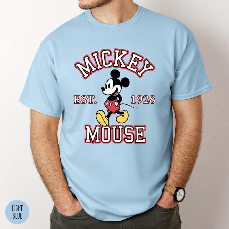A man wearing a light blue tee with a classic Mickey Mouse graphic and text reading "Mickey Est. 1928 Mouse" in red and white lettering.