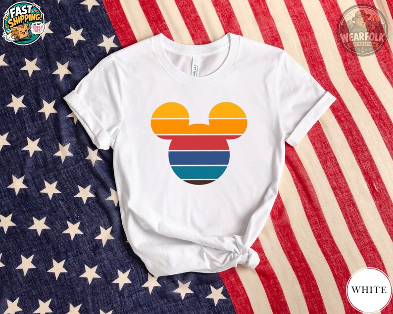 White tee with a colorful Mickey Mouse head silhouette featuring orange, red, navy, teal, and brown horizontal stripes.