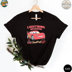 Black Bella Canvas tee with a red Lightning McQueen race car graphic and text reading "Lightning McQueen est. 1977 Ultimate Speed Think Fast Radiator.