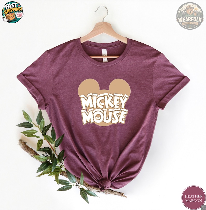 Heather maroon tee with tan Mickey Mouse ears and white outlined text reading "MICKEY MOUSE" across the chest.
