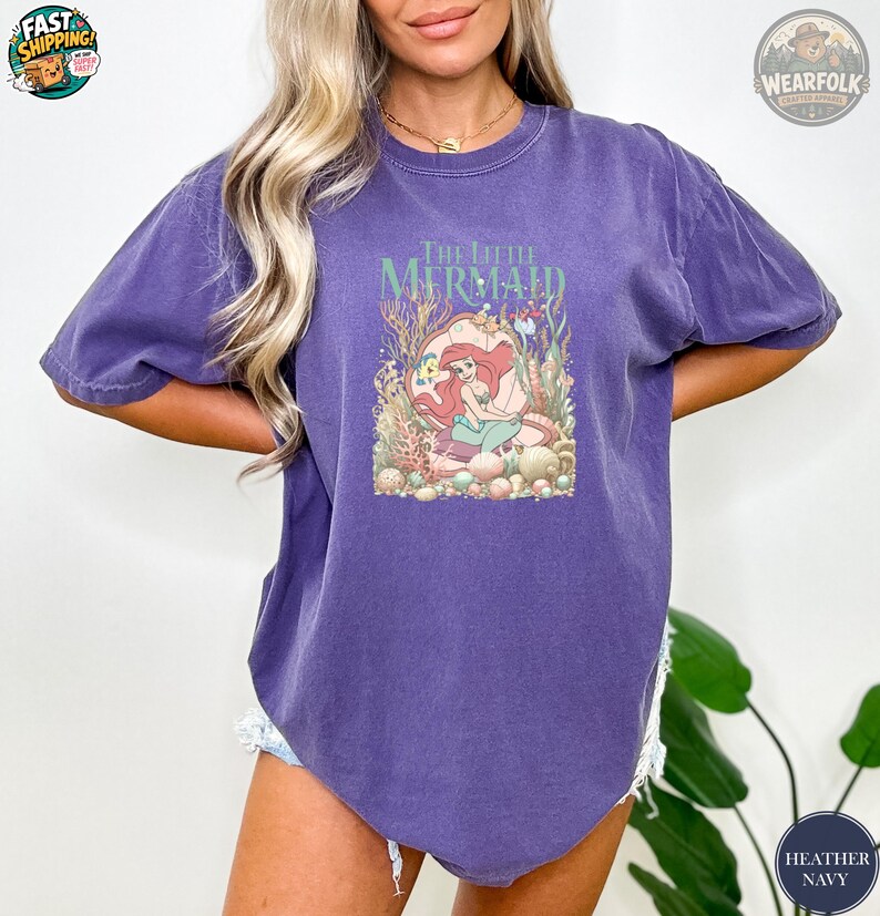 A woman wearing a purple vintage tee with The Little Mermaid graphic featuring Ariana character surrounded by colorful coral and sea creatures.