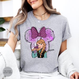 Woman wearing a heather gray tee with Anna from Frozen inside a purple mouse ear head silhouette with sparkles and the name "Anna" printed below.