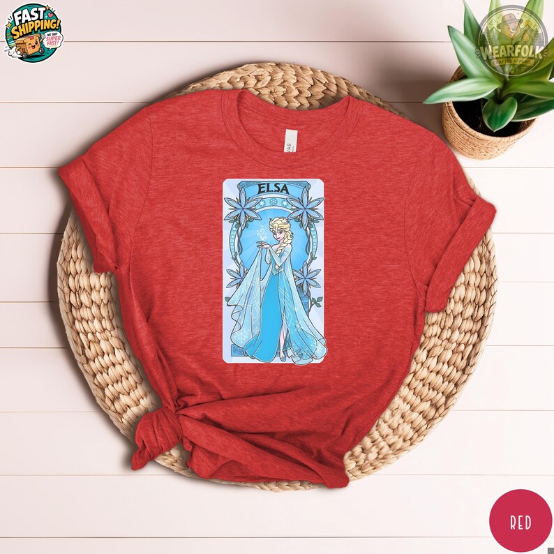 Red Bella Canvas tee featuring a centered graphic of Elsa in a blue ice dress surrounded by snowflake designs with her name at the top.