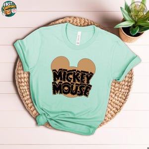 Mint green Bella Canvas tee with Mickey Mouse ears graphic and black and gold "Mickey Mouse" text on the chest.