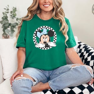 A woman wearing a green tee with a checkered circle graphic of Minnie Mouse wearing a blue bow.