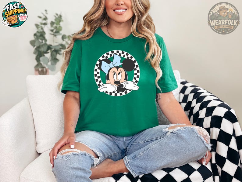 A woman wearing a green tee with a checkered circle graphic of Minnie Mouse wearing a blue bow.