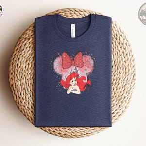 Navy Bella Canvas tee with a graphic of Ariel's face with red hair and a red polka dot bow, surrounded by pink watercolor and castle details.