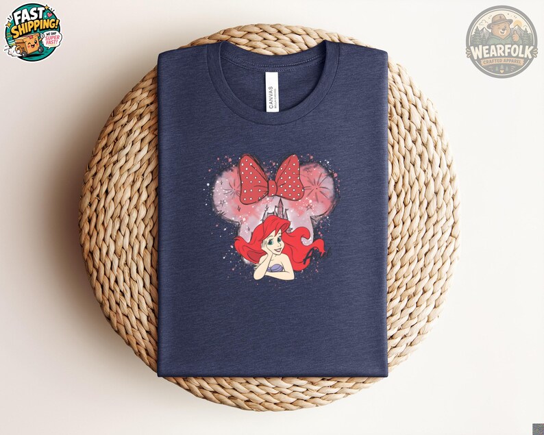 Navy Bella Canvas tee with a graphic of Ariel's face with red hair and a red polka dot bow, surrounded by pink watercolor and castle details.