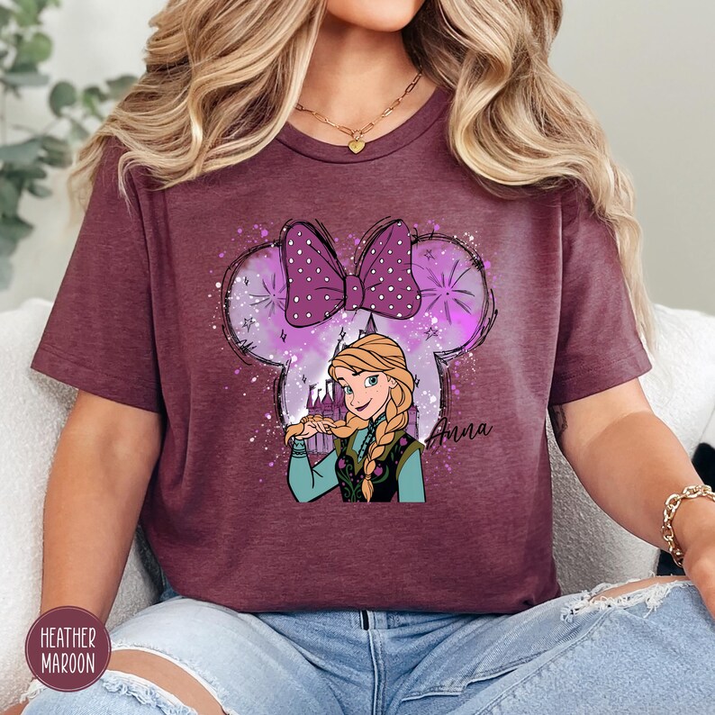 Woman wearing a heather maroon tee with Anna from Frozen inside a Mickey ear silhouette with sparkles and the text "Anna".