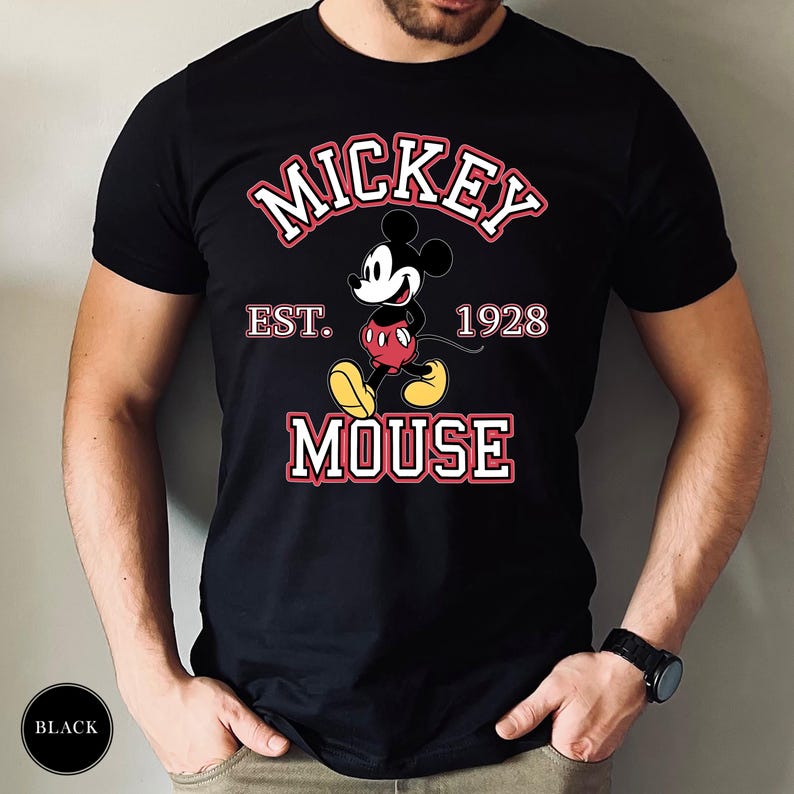 A man wearing a black tee with a Mickey Mouse graphic and text reading "Mickey Est. 1928 Mouse" in red and white lettering.