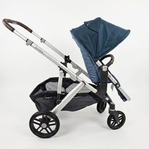 May include: A modern stroller with a navy blue canopy and seat. The stroller has a silver frame, black wheels, and a brown handle. The word "VISTA" is printed on the frame.