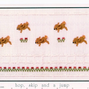 May include: A cross-stitch pattern featuring five brown bunnies hopping over a row of green leaves and red flowers. The pattern is titled "hop, skip and a jump".