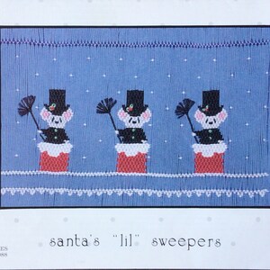 May include: Cross-stitch pattern featuring three mice dressed as chimney sweeps, wearing top hats and holding brooms. They stand atop red brick chimneys against a blue background with falling snow. The text "santa's 'lil' sweepers" is below the image.