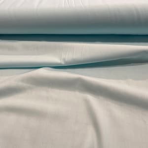 May include: A roll of light blue fabric with a smooth, even texture. The fabric is folded in half and has a slight sheen.
