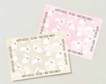 May include: Two rectangular greeting cards featuring a repeating pattern of white bunnies with small bows on a watercolor background. One card is light pink and the other is beige. Both cards have the text HAPPY EASTER - TO YOU - AND YOUR FAMILY printed along the borders.
