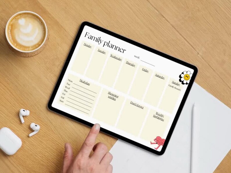 May include: A digital family planner displayed on a tablet, featuring sections for each day of the week, meal plans, and reminders. A cup of coffee and wireless earbuds are next to the tablet on a wooden surface.