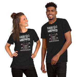 May include: Two people wearing dark gray t-shirts. The shirts feature the text "Isaiah 63:3 I Tread the Winepress Alone" above a graphic of a wine press. The graphic is in red, white, and gray. The shirts are short-sleeved.