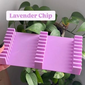 May include: A lavender-colored chip holder with a rectangular base and vertical dividers. The text "Lavender Chip" is displayed on a white background. The holder is held in front of a background of green plants.