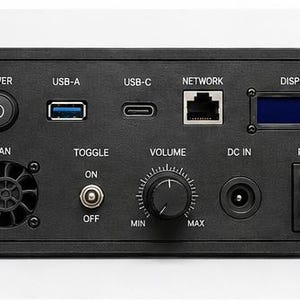 May include: A black rectangular control panel featuring a power button, USB-A and USB-C ports, a network port, and a small display screen. Below are a cooling fan, an on-off toggle switch, a volume knob labeled MIN to MAX, a DC IN port, and a rocker switch.
