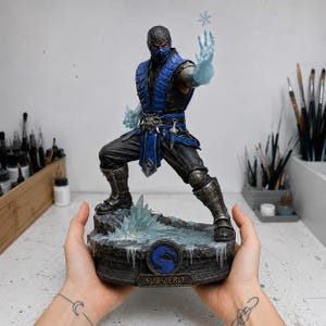 May include: A detailed Sub-Zero figurine standing on a rocky, icy base. The character wears a black and blue outfit with metallic armour accents, holding a translucent blue ice effect with a snowflake in one hand and ice on the other hand.